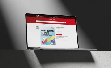 A laptop is positioned on a table, showing the TUC shop website.