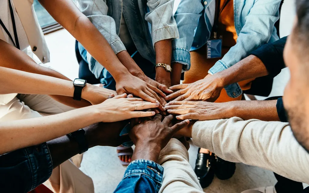 A diverse group of people standing together with their hands joined in a gesture of unity and collaboration.